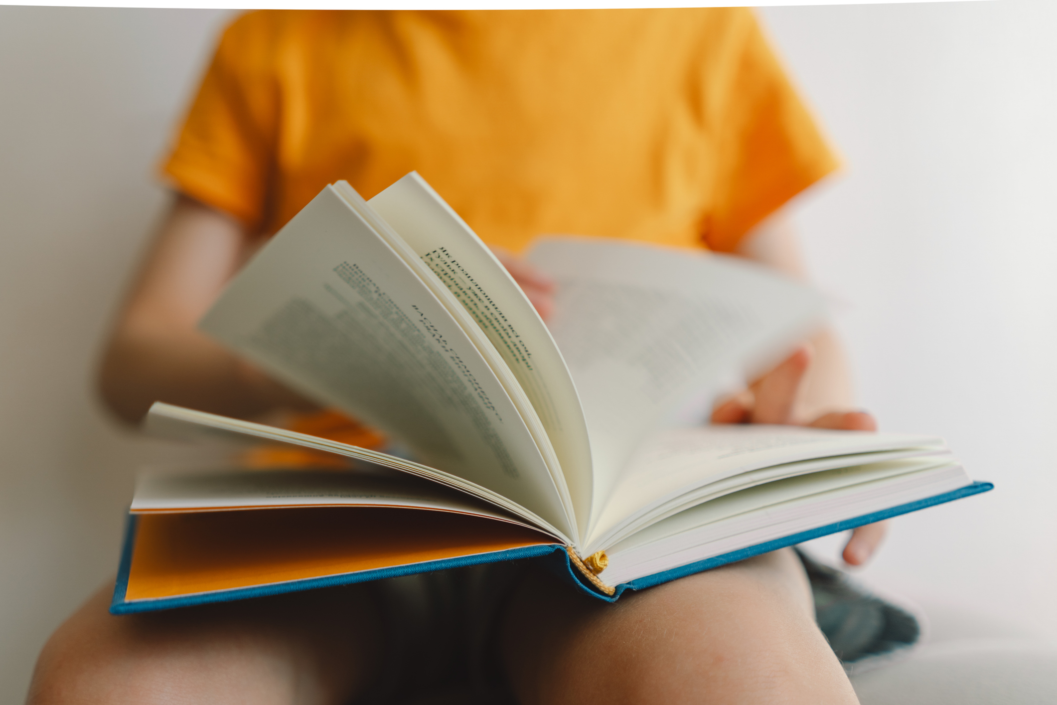 A cute boy is sitting on a soft ottoman reading a book.